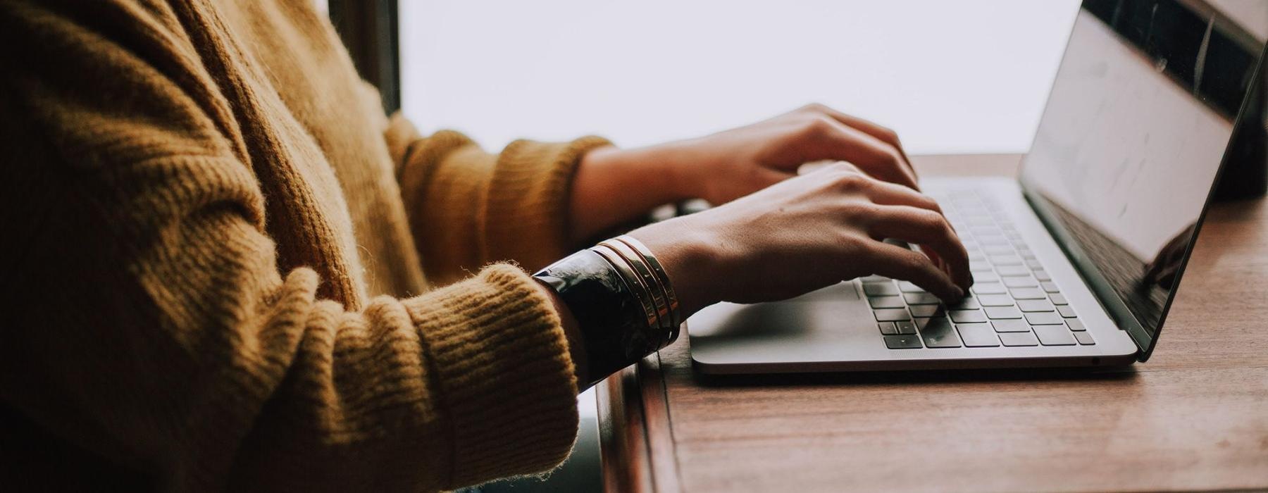 woman types on her laptop near large window
